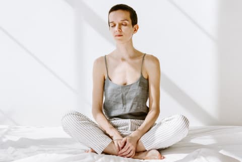 Young woman sitting on a bed with her eyes closed meditating