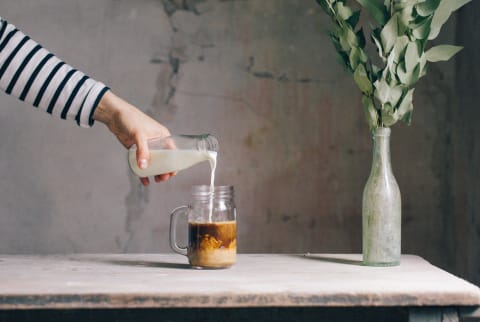 milk pouring into a glass of ice coffee milk pouring into a glass of ice coffee
