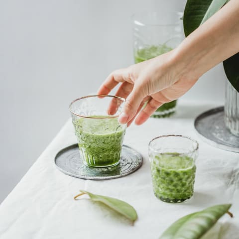 Hand Reaching for a Glass of Green Juice