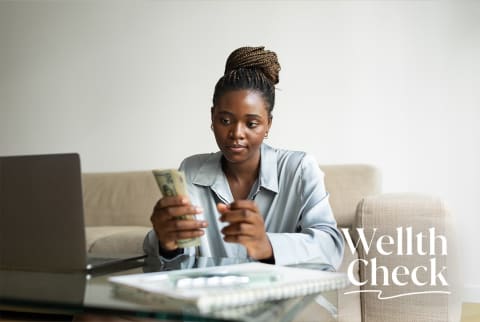 woman in boue button down checking her phone sitting at a desk in front of a computer