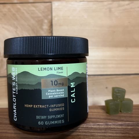 Best CBD Gummies for Sleep Charlottes Web  on wood backround next to stack of gummies